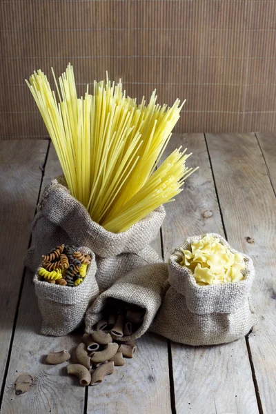 Verschiedene Formen von Pasta in Jutesäcken auf Holztisch — Stockfoto