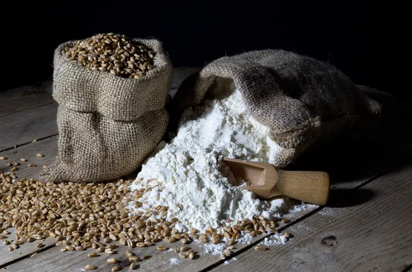 Jutesäcke gefüllt mit Weizen und Mehl auf einem alten Holztisch auf schwarz — Stockfoto