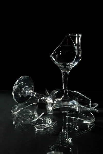 Gebroken wijnglazen met reflectie op een glazen tafel geïsoleerd op zwart — Stockfoto