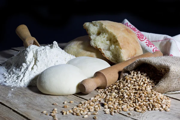 Mehl, Teig, Brot, Nudelholz und Jutebeutel gefüllt mit Weizen auf rustikalem Holztisch auf schwarzem Hintergrund — Stockfoto