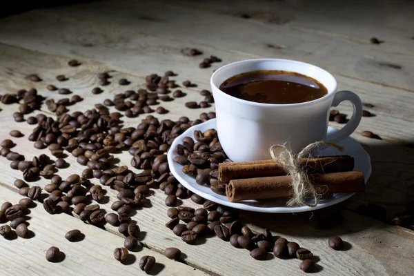 Tazza di caffè bianco e piattino con cannella e chicchi di caffè sul tavolo di legno — Foto Stock