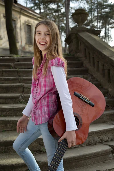 Menina sorridente amigável despreocupada com guitarra em sua mão Olhando para a câmera ao ar livre — Fotografia de Stock