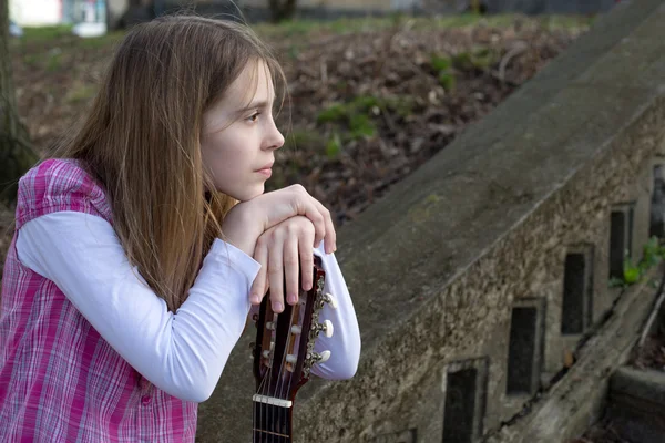 Vue latérale de la jeune fille rêveuse s'appuyant sur sa guitare extérieure — Photo