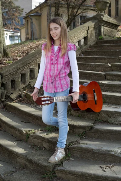 Adolescente souriante avec guitare dans sa main descendant les vieux escaliers en pierre à l'extérieur — Photo