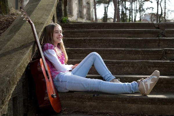 Garota sorridente com guitarra sentada nas escadas no parque e descansando na ensolarada Primavera da Europa — Fotografia de Stock