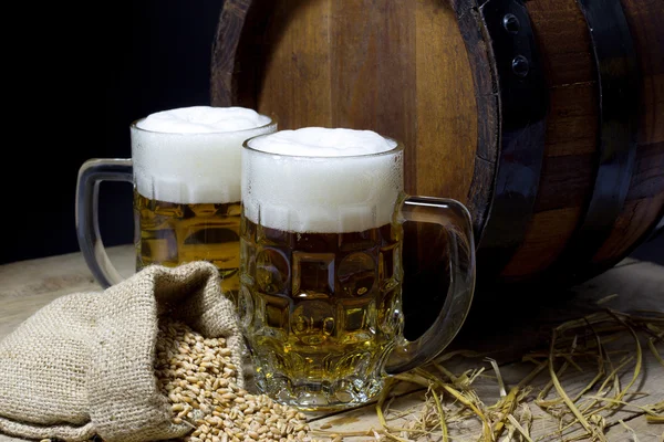 Két csésze hideg sör, a hordó és a juta zsák búza a fekete fából készült asztal tele — Stock Fotó