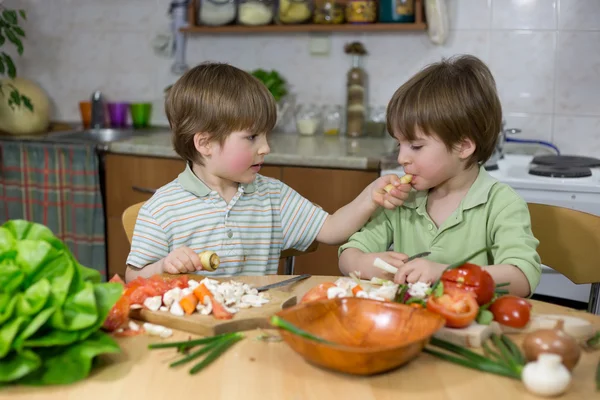 Cute Little Boy Feeding His Twin Brother With Parsnip at Kitchen Table