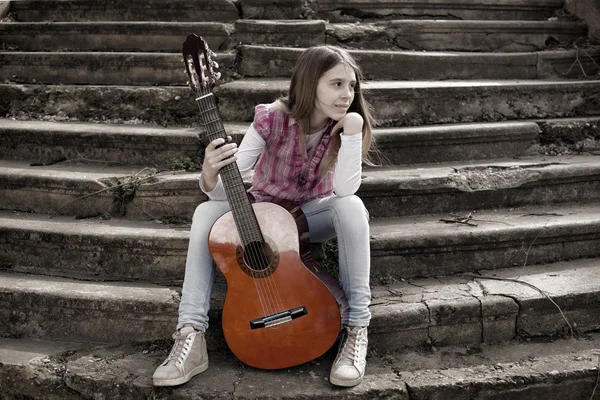 Jeune fille avec guitare assise au pied des escaliers et regardant loin — Photo