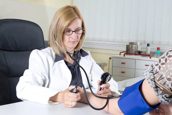 Misurazione della pressione sanguigna da parte del medico con stetoscopio e sfigmomanometro nella sala di consultazione — Foto Stock