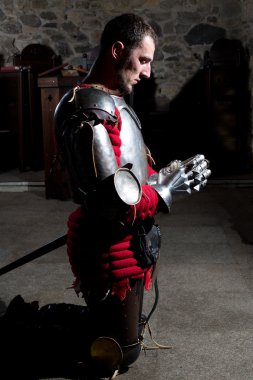 Başını dizlerinin üzerine diz çökmüş Knight yan görünüm eğdi ve eski kilisede dua eller