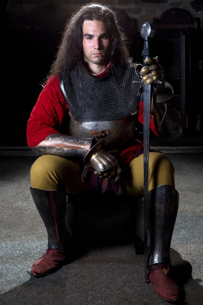 Лобовой вид рыцаря с мечом, сидящего на каменной стене — стоковое фото