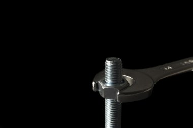 Metal Spanner Gripping And Turning Nut Around Metal Bolt Isolated On Black Background clipart