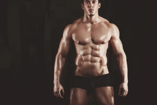 Nahaufnahme eines jungen muskulösen Mannes, der Gewichte vor dunklem Hintergrund stemmt — Stockfoto