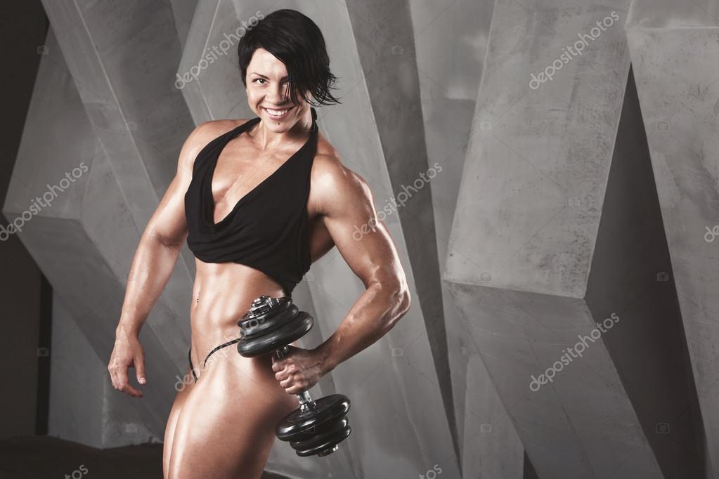 Athletic woman pumping up muscules with dumbbells Stock Photo by