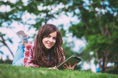 Kadın parkta tablet ile yeşil çim üzerinde yalan.
