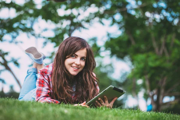 Kadın parkta tablet ile yeşil çim üzerinde yalan.