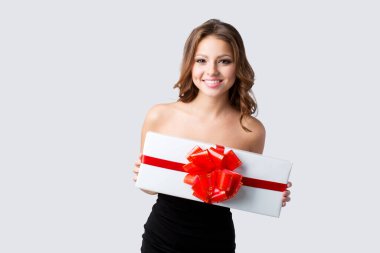 Gri arka planda kırmızı fiyonklu beyaz hediye kutusu taşıyan siyah elbiseli güzel bir kadın..