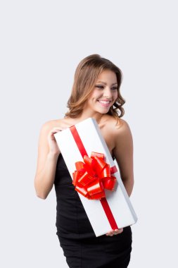Siyah elbiseli mutlu kadın gri arka planda kırmızı kurdeleli beyaz bir kutu tutuyor..