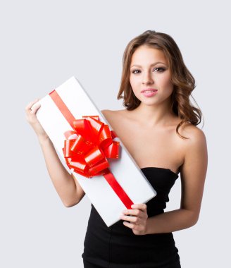 Siyah elbiseli çekici bir kadın gri arka planda kırmızı kurdeleli beyaz bir kutu tutuyor..