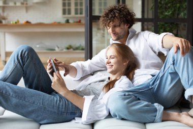Birbirine aşık çiftler evlerinde dijital tablet kullanarak kanepede dinlenirler. İnternetten alışveriş.