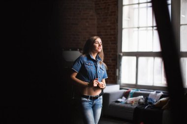 Güzel, gülümseyen bir kadın modern bir çatı katında kot elbise giyiyor..