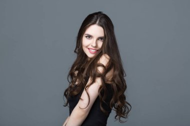 Stüdyoda gri arka planda poz veren uzun dalgalı saçlı güzel bir kadın..