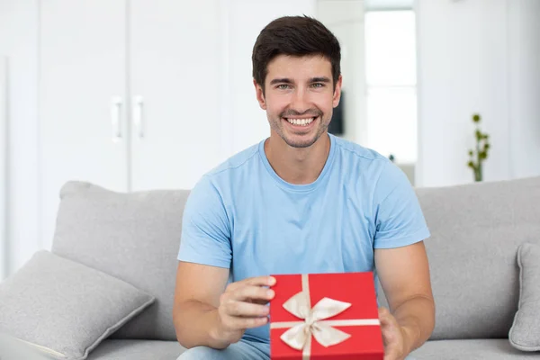 Joven Hombre Guapo Sonriente Con Regalo Sus Manos Sienta Sofá — Foto de Stock