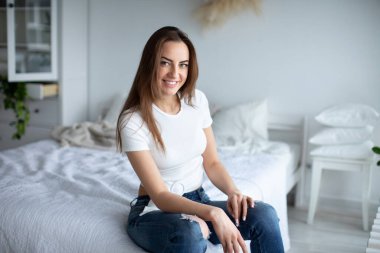 Gülümseyen genç kadın evde dinleniyor. Esmer kadın, günlük giysiler giyiyor ve içeride kameraya bakıyor..