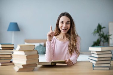 Bir sürü kitapla masada oturan mutlu kız öğrenci başparmağını kaldırıp sınavlara hazırlanıyor..
