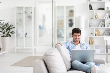 Enjoying time at home. Handsome young man sitting on the couch In a living room with laptop.