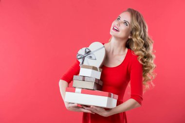 Kırmızı elbiseli güzel bir kadın pembe arka planda sevgililer günü için bir sürü hediye kutusu tutuyor..