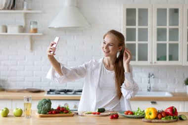 Mutlu kadın, taze sebzeler hazırlarken selfie çeker. Evde kalır, sağlıklı yemekler yer..