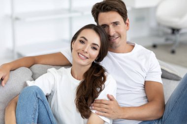 Mutlu çift evdeki rahat bir kanepede oturuyor. Sarılmak, gülümsemek ve kameraya bakmak..