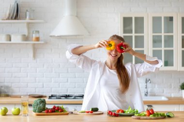 Genç bir kadın mutfakta eğlenirken taze sebzeler hazırlıyor evde oturup sağlıklı yemekler yiyor..