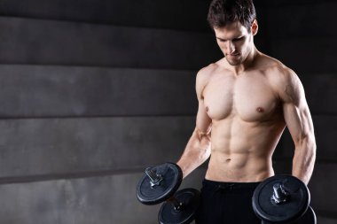 Koyu arkaplanda dambılı tişörtsüz bir atletizm portresi. Stüdyo çekimi.