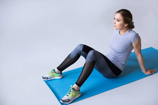 身穿蓝色瑜伽垫运动服的女性在运动结束后 在灰色背景下看着摄像机休息 — 图库照片