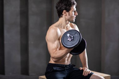 Güçlü kaslı adam ağır halterlerle oturur ve kaslarını çalıştırır. Vücut geliştirme ve sağlıklı yaşam tarzı konsepti.