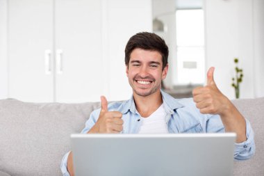 Dizüstü bilgisayarı olan mutlu bir adam başparmağını kaldırıyor ve gülümseyerek onayını veriyor..