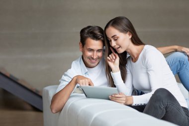 Mutlu çift iving odasında tablet bilgisayar kullanıyor, internetten hizmet seçiyor, online alışveriş yapıyor..