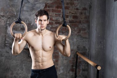 Eski bir tuğla duvarın arka planında jimnastik yüzükleriyle yakışıklı sporcu..