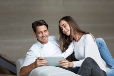 Elektronik tablet kullanan neşeli çift evdeki oturma odasında oturuyor. İnternet ve çevrimiçi alışveriş hizmetlerini seçin.