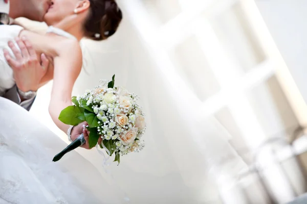 Dia do casamento. A noiva beija o noivo segurando buquê de noiva — Fotografia de Stock
