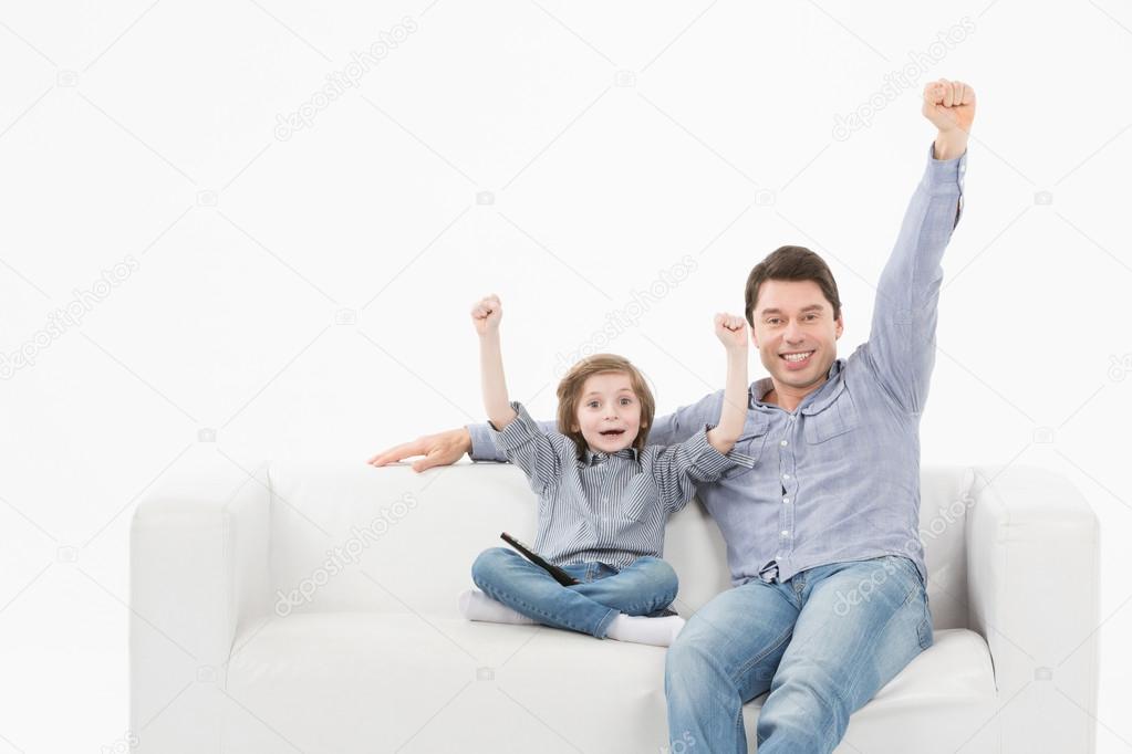 smiling man and son watching sports on tv and supporting team at home