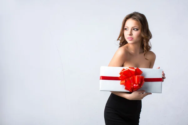Mujer en un vestido negro sosteniendo una caja blanca con un lazo rojo y cinta . — Foto de Stock