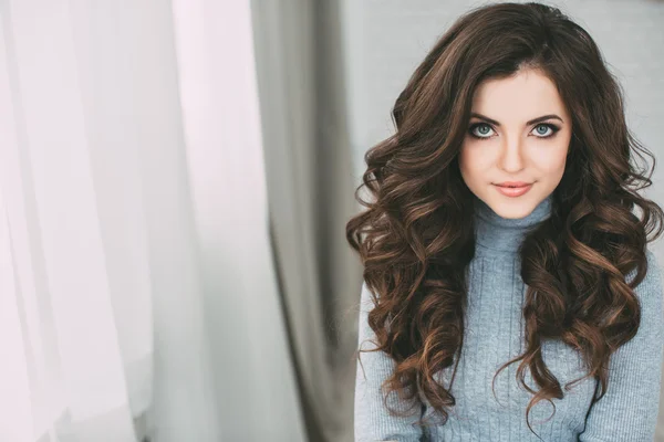 Portrait young beautiful brunette with long curly hair at home.