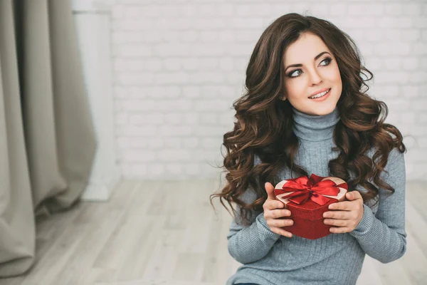 Hermosa mujer con cabello largo rizado sosteniendo el corazón de la caja de regalo y mirando a la cámara . — Foto de Stock
