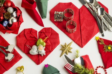 Farklı şekillerde katlanmış, kırmızı ve yeşil renkli kağıt peçeteler beyaz üzerine çatal bıçak seti ve tabakla birlikte. Noel ya da yeni yıl ziyafeti için hazırlık. Peçetelerin genel görünümü.