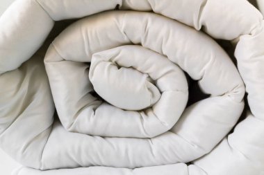 Yumuşak, beyaz, yıkanabilir çift katlı fiber yorgan beyaz arka planda yuvarlandı. Yakın plan alındı..