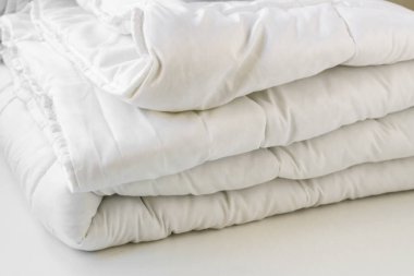 Yumuşak, beyaz, yıkanabilir çift katlı fiber yorgan beyaz arka planda yuvarlandı. Yakın plan alındı..