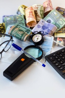 Kırpılmış Avro, ABD Doları ve Türk Banknotları klasik alarm saati, hesap makinesi, kalem, büyüteç ve tıbbi maskeler ile beyaz üzerine.